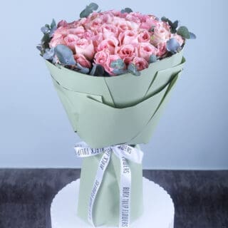 Elegant pastel pink roses arranged with eucalyptus, wrapped in stylish sage green paper.