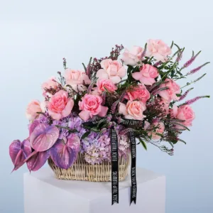 A lush and artfully arranged floral basket is presented, filled with a variety of delicate pink and purple flowers and verdant foliage