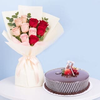 A celebration combo featuring a bouquet of red and pink roses, a round chocolate cake with white stripes and strawberries on top..