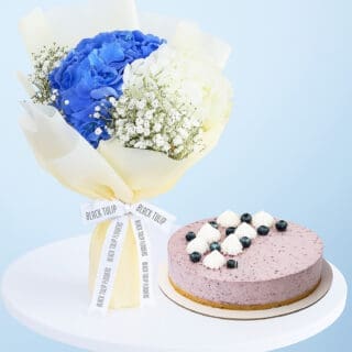 A flower combo featuring a bouquet of blue and white hydrangeas and baby's breath wrapped in cream and a purple-colored cheesecake.