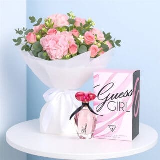 A Guess Girl EDT for Women with a White-wrapped bouquet of blush hydrangea, pink spray roses, and greenery on a table.
