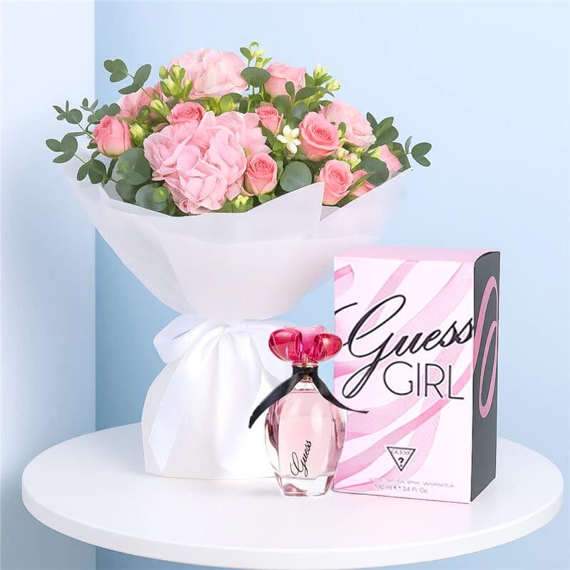 Guess Girl with Pink Hydrangea & Spray Roses-01-030-25 A Guess Girl EDT for Women with a White-wrapped bouquet of blush hydrangea, pink spray roses, and greenery on a table.