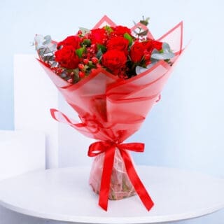 A bouquet of red roses, eucalyptus leaves and red hypericum in a bold red translucent wrapping.