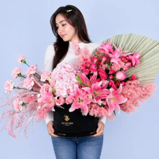 A stunning pink floral arrangement featuring fresh blooms is carefully set up inside a premium black box, designed to offer a luxurious and elegant presentation.