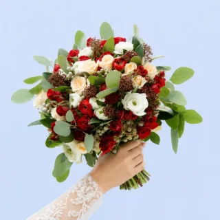 Sophisticated bridal bouquet with crimson ranunculus, peach spray roses, white florals, brunia details, and layered garden-inspired foliage.