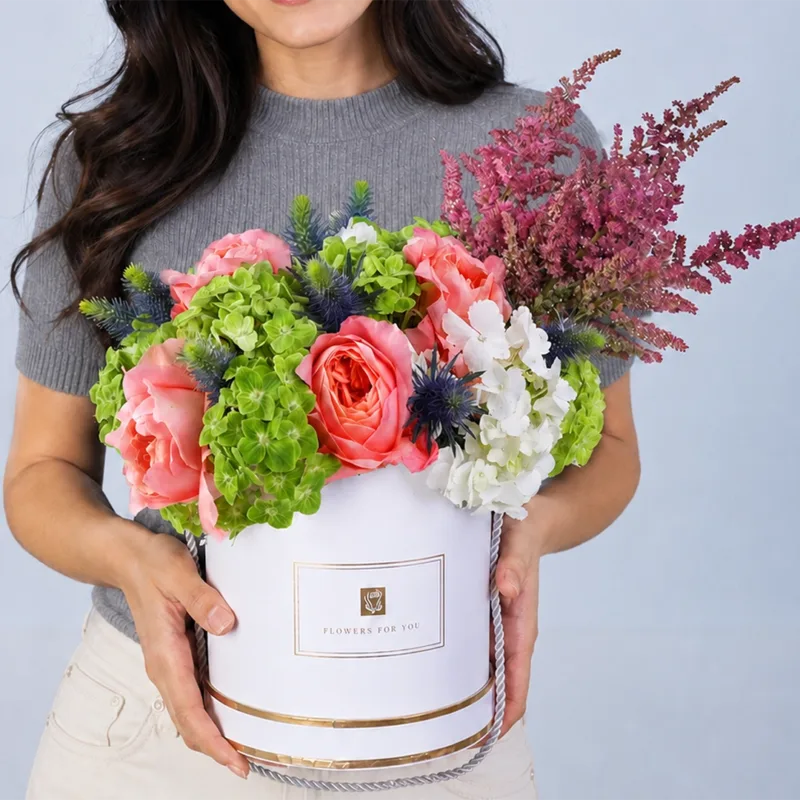 luxe-blossom-eid-gift-box-2026_new Luxury flower arrangement with peach roses, white hydrangeas, green hydrangeas, blue eryngium, and red astilbe in a white round box.