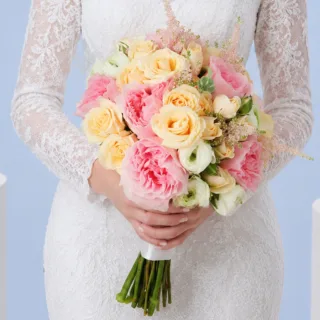 Modern romantic bridal bouquet featuring pastel roses, white ranunculus, peach spray roses, and soft pink astilbe stems, all combined together as a bridal bouquet.