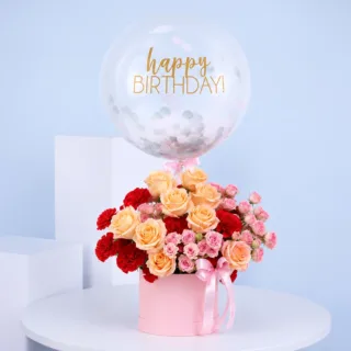 Elegant birthday gift flower box containing peach roses, red carnations, pink spray roses, and a happy birthday balloon.