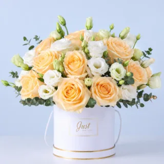 A charming arrangement of peach and pink roses with delicate buds in a white round box crafted into an elegant floral gift.