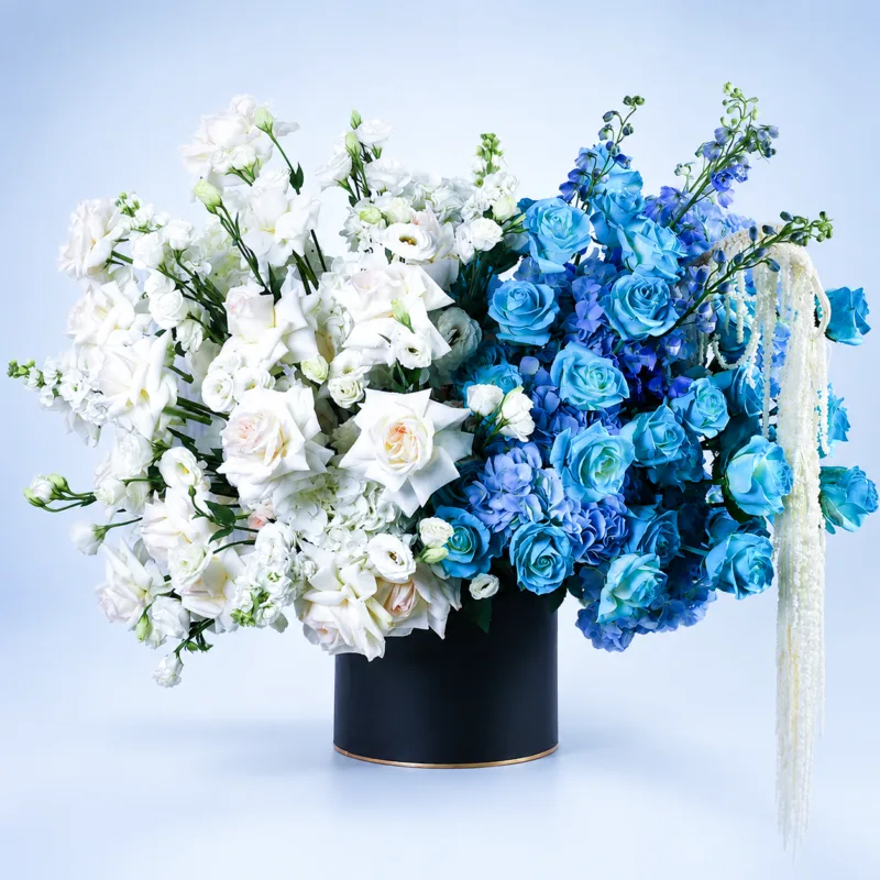blue-white-luxury-hat-box Blue & White Luxury Hat Box featuring fresh blue painted roses, White O'Hara roses, white matthiola, blue and white hydrangeas, blue delphiniums, white lisianthus, and dried amaranthus beautifully arranged in a premium black hat box for gifting and special occasions.
