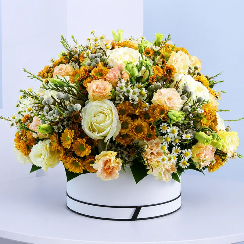 golden-bloom-floral-hat-box Golden Bloom Floral Hat Box featuring fresh orange santini chrysanthemums, white roses, peach lisianthus, brunia, white tanacetum, and white wax flowers beautifully arranged in a premium white hat box for gifting and special occasions.