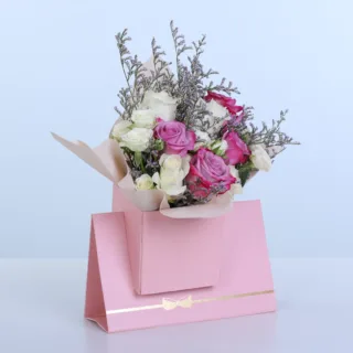 Purple & White Rose Pink Envelope Box featuring 5 purple roses, 5 white roses, 3 spray roses, and delicate caspia arranged in a premium pink envelope-style flower box.