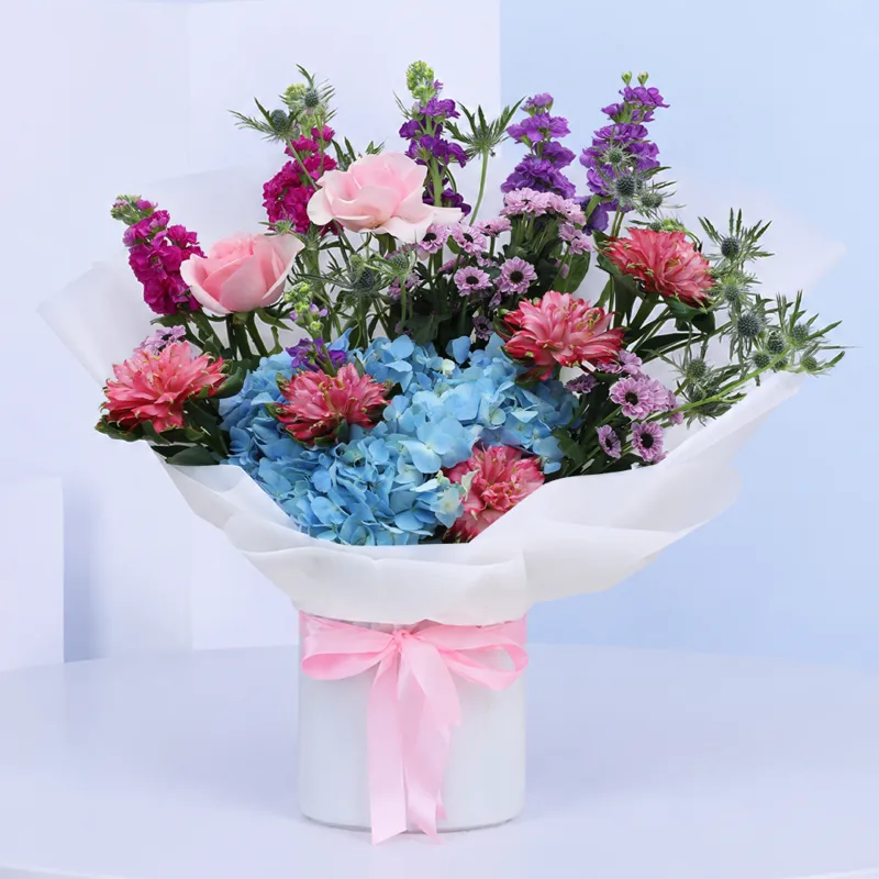 radiant-mixed-bloom-bouquet Radiant Mixed Bloom Bouquet featuring pink matthiola, purple matthiola, blue hydrangeas, red alstroemeria, and green eryngium arranged in a colourful hand-tied flower bouquet.