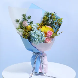 Pastel Garden Bloom Bouquet featuring blue hydrangeas, light pink roses, white matthiola, yellow blooms, eryngium, and anigozanthos beautifully arranged in elegant wrapping.