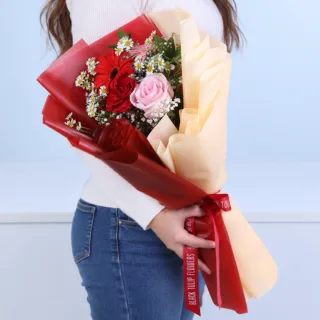 Red and pink garden bloom bouquet featuring red roses, pink roses, red gerbera, pink gerbera, tanacetum, white gypsophila, and ruscus, beautifully arranged for celebrations and thoughtful gifting occasions.