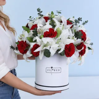Crimson Pearl Flower Box featuring red roses, white Oriental lilies, and Baby Blue eucalyptus in a white hatbox.