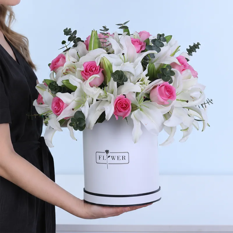 Gentle Grace featuring pink roses, pink Oriental lilies, and Baby Blue eucalyptus arranged in a white hatbox.