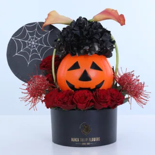 Haunted Pumpkin Halloween flower arrangement featuring seven red roses, two orange calla lilies, two painted hydrangeas, and Cordifolium foliage with a pumpkin centrepiece and spiderweb decoration.