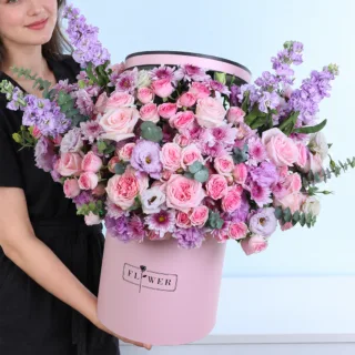 Pink Twilight flower box featuring light pink roses, peach Sweet Sara baby roses, pink Dinara baby roses, Malibu chrysanthemums, purple matthiola, lisianthus, and eucalyptus.
