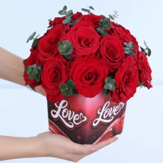 Romance Overloaded red rose arrangement featuring 18 vibrant red roses and Baby Blue eucalyptus in a Love-themed glass cube vase.