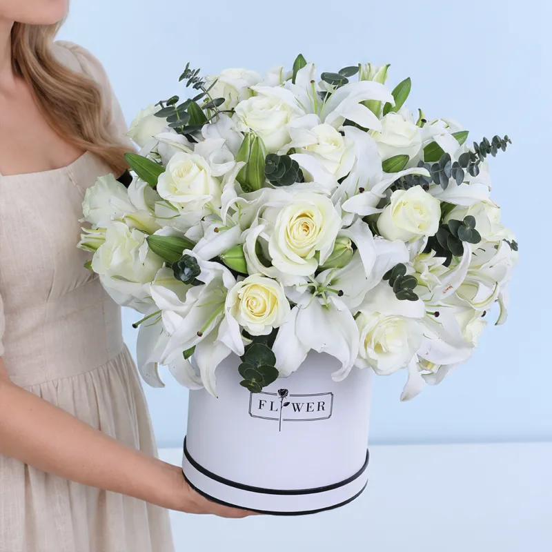 Snowy Floral Whispers featuring white roses, white Oriental lilies, and Baby Blue eucalyptus in a white hatbox.