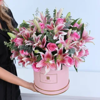 Whispers of Pink featuring pink roses, pink Oriental lilies, and Baby Blue eucalyptus in an elegant pink hatbox.