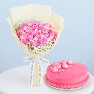 BTF Home 101 A flower combo featuring a bouquet of pink hydrangeas with baby's breath wrapped in cream and tied with a black and white ribbon with a round pink frosted cake.