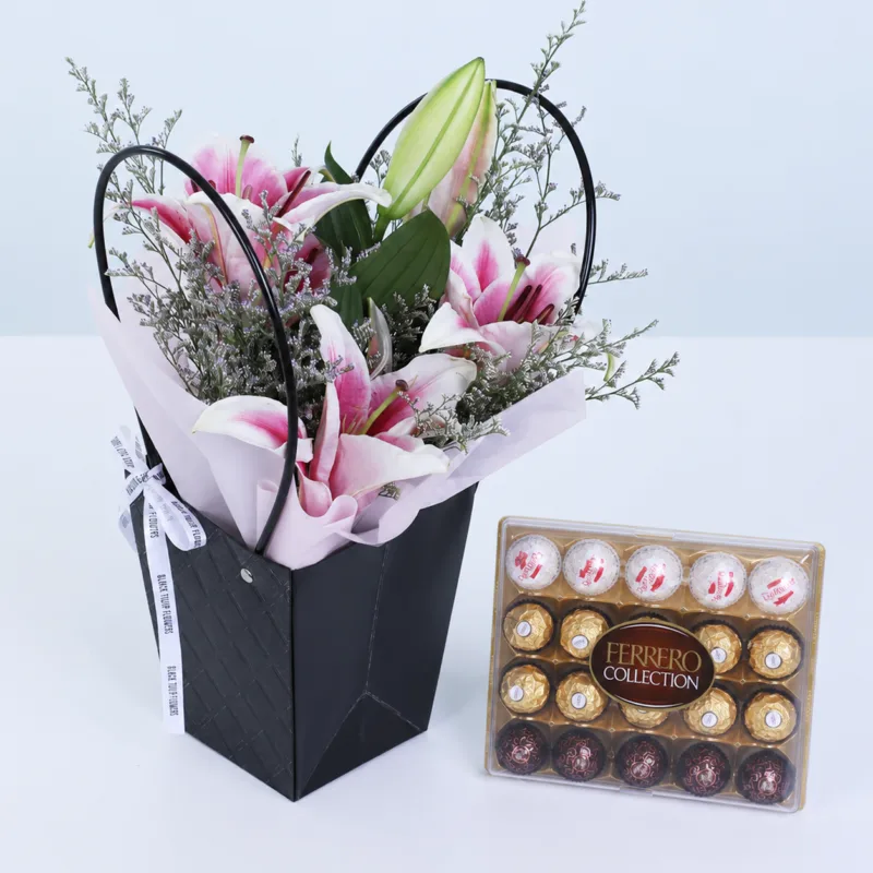 pink-lily-floral-bag-with-ferrero-collection Pink Lily Floral Bag with Ferrero Collection featuring 2 fresh pink lily stems, 3 stems of delicate caspia, and Ferrero Collection chocolates arranged in a premium black floral bag for gifting and special occasions.